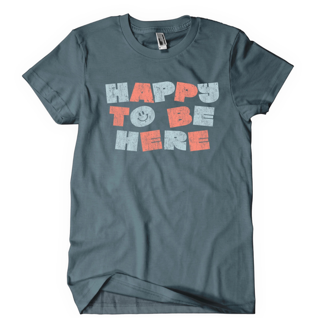 Blue grey shirt says, "Happy To Be Here" screen printed in light blue and pink ith smiley face. 
