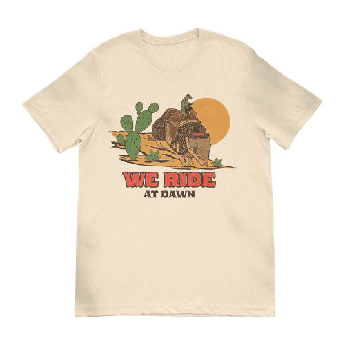 Tan shirt with lizard riding an armadillo says, "We Ride at Dawn" in western font. 