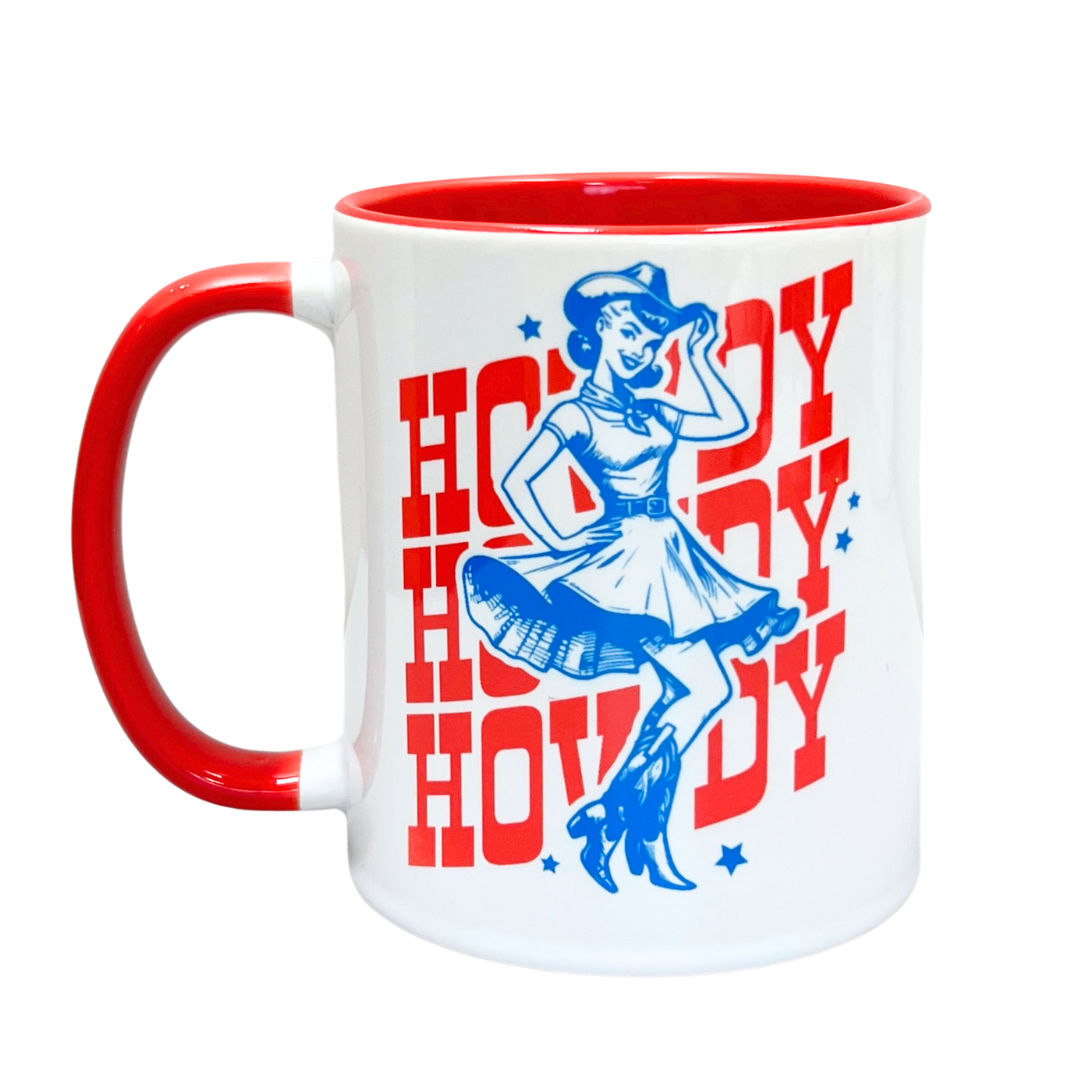 Mug features a cowgirl wearing boots, a southern belle dress, and a cowboy hat. Behind her is "Howdy" three times. White base. Handle is red. Inside of mug is red. 11 oz.