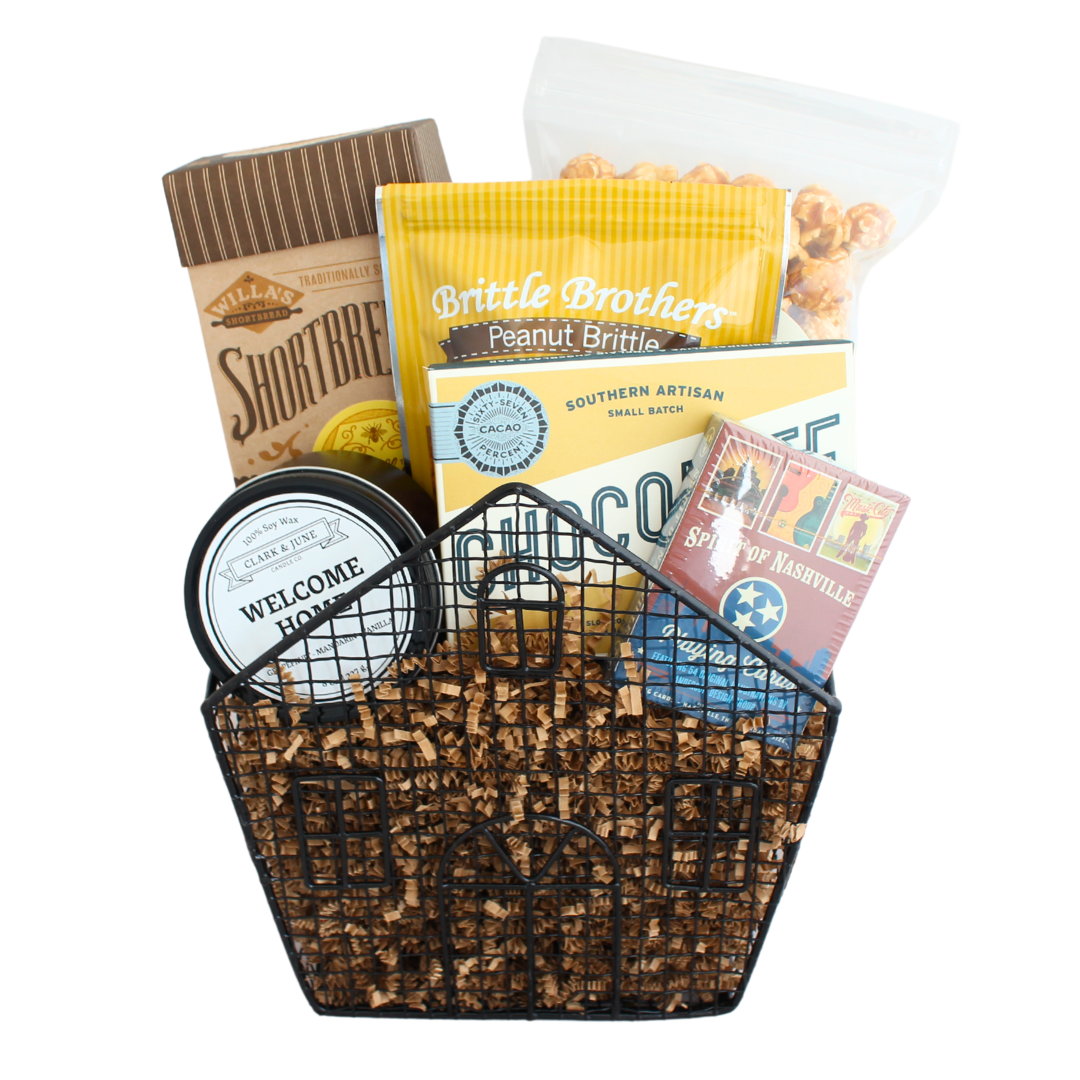 collection of snacks, a candle and playing cards in wire house shaped basket. 