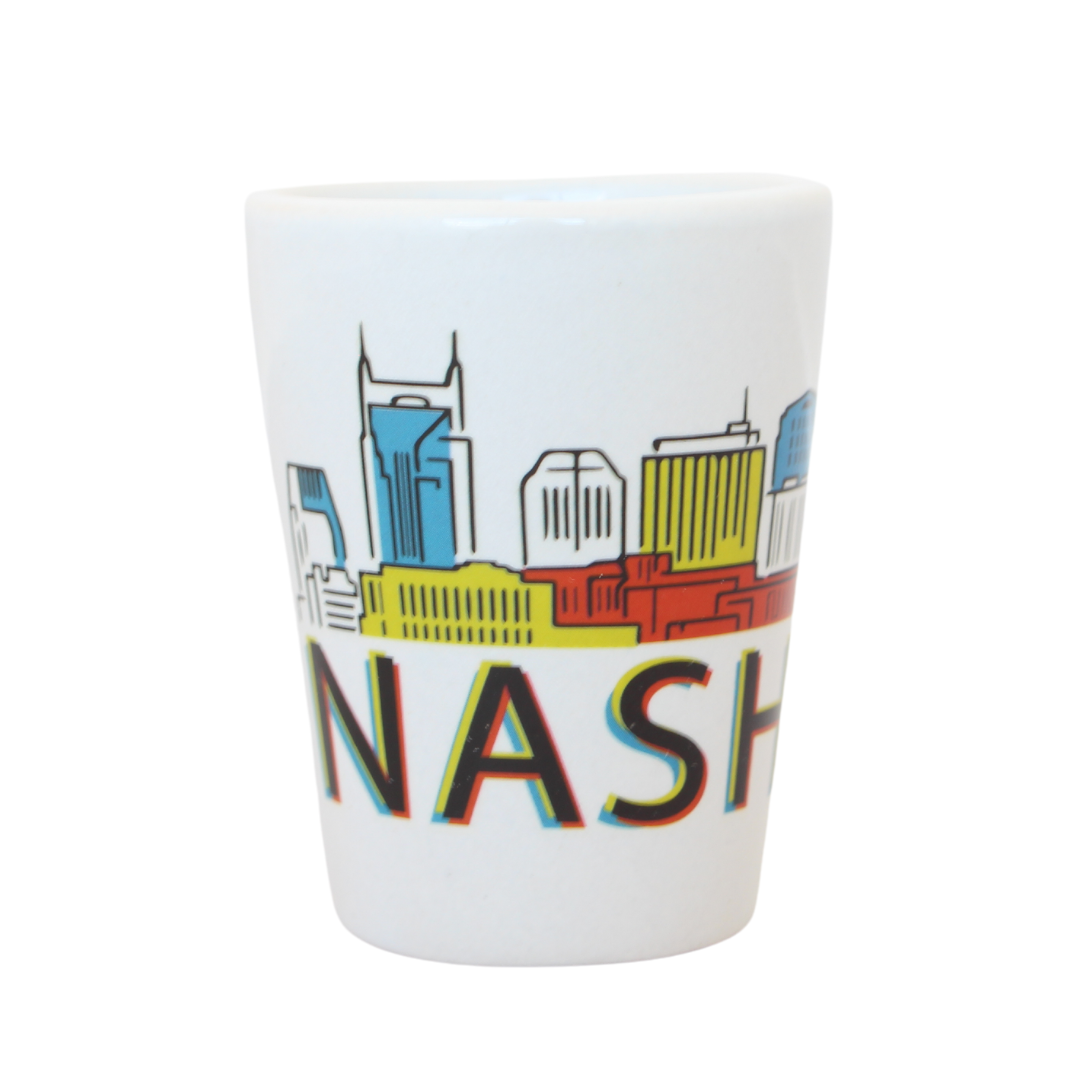 White shot glass with illustration of Nashville skyline in primary colors.